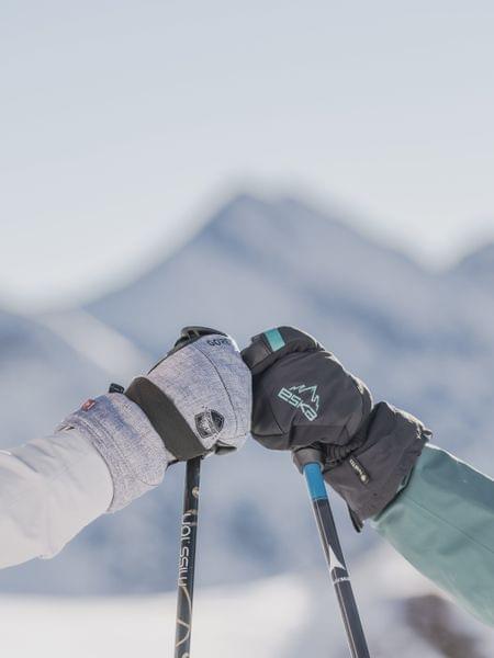 Skiopening Obertauern Zwei Skifahrerinnen begrüßen sich mit Skistöcken vor verschneiten Bergen